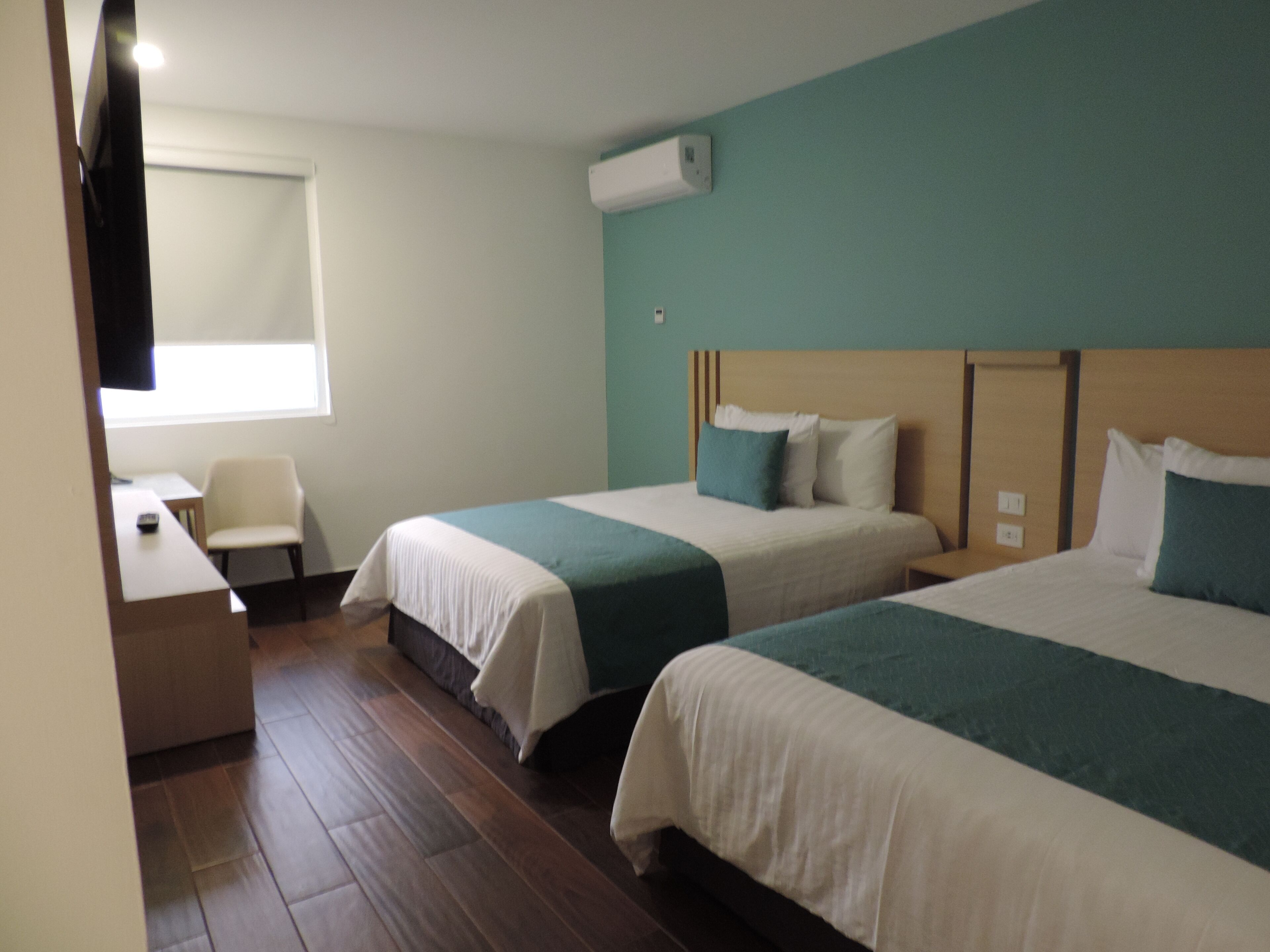 Una habitación de hotel con dos camas, un escritorio, una silla y una ventana.