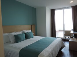 Habitación de hotel con una cama grande, cabecera de madera, escritorio y vista al exterior por una puerta corrediza.