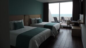A hotel room with two beds, a desk, and a view of the ocean.