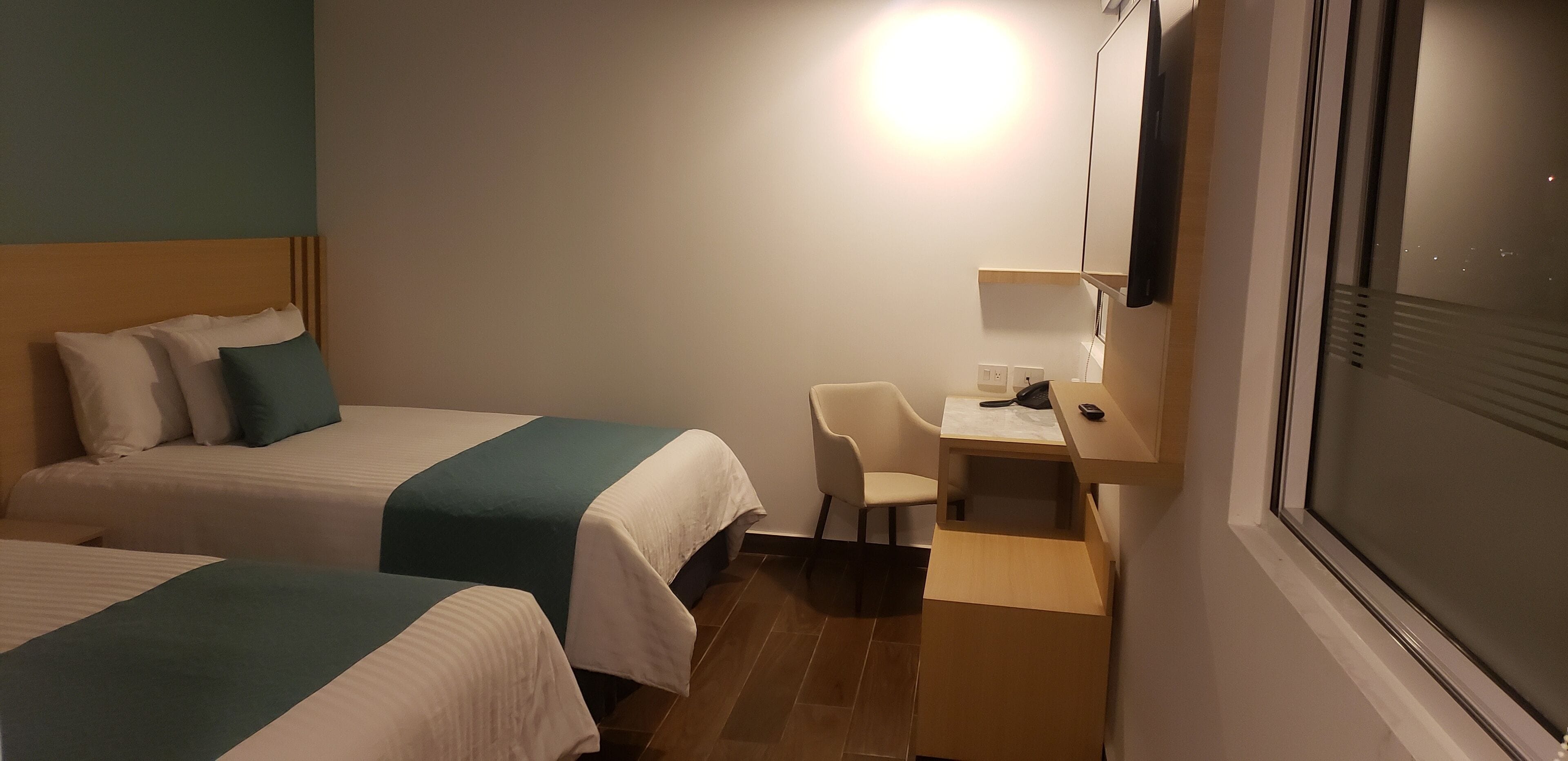 Habitación de hotel con dos camas, un escritorio, una silla y una ventana.