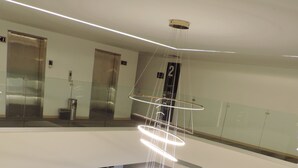 A modern lobby with a high ceiling, a unique light fixture, seating areas, and a glass railing overlooking the space.