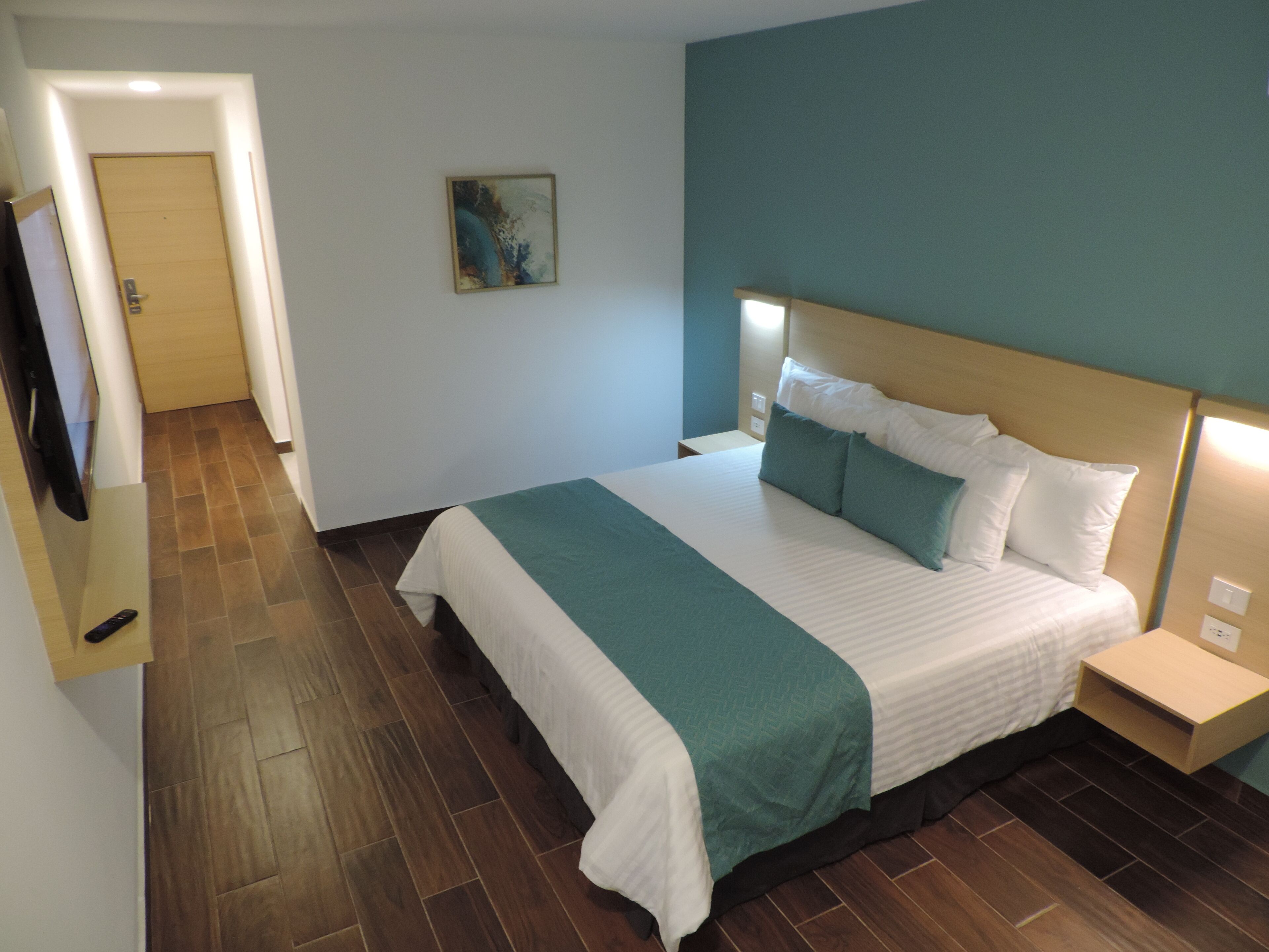Habitación de hotel con una cama grande, suelo de madera, pared de acento color aguamarina y un cuadro en la pared.