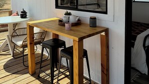A wooden deck with a table and chairs, a window with a view, and a sign on the wall. - Comfy Cottage With Writer Cabin and Book Nook. Pet-Friendly Fully Fenced Yard (Joshua Tree)