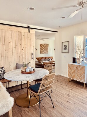 A modern living room with a round marble table, wicker chairs, a sofa, and a wooden cabinet. - Comfy Cottage With Writer Cabin and Book Nook. Pet-Friendly Fully Fenced Yard (Joshua Tree)
