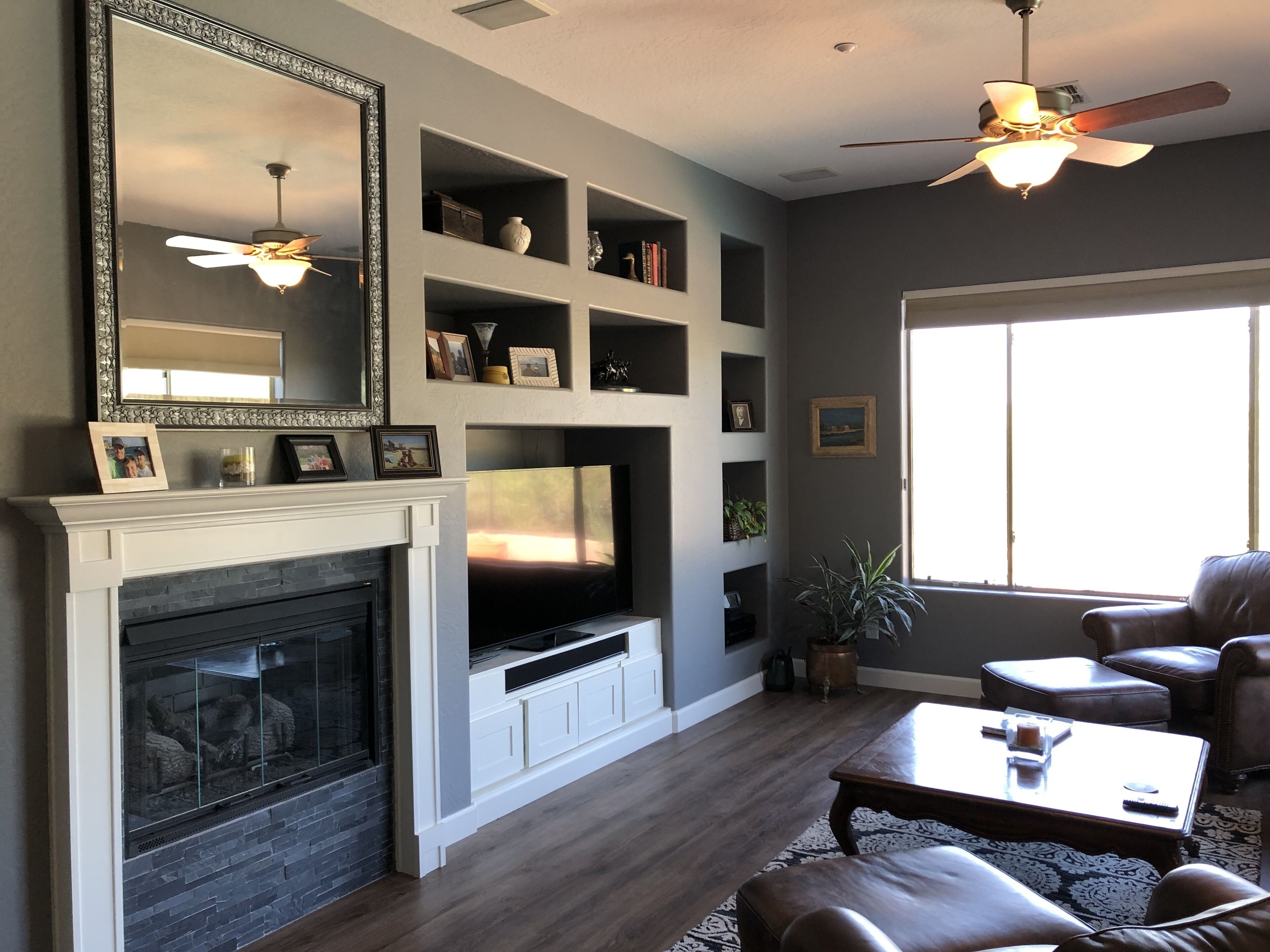 A living room with a fireplace, a large mirror, a television, and a ceiling fan.
