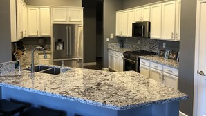 A modern kitchen with white cabinets, a stainless steel refrigerator, a built-in oven, and a granite countertop.