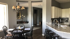 A modern kitchen with a marble island, dark wood flooring, and a dining area with a chandelier.