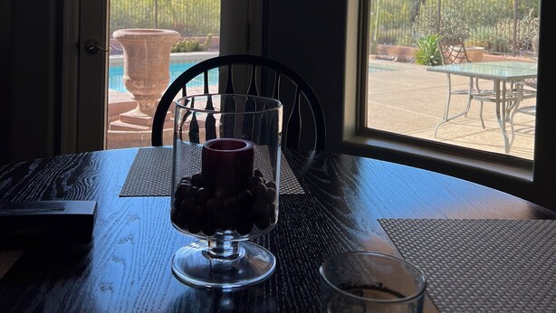 A table with a laptop, a glass of water, and a glass of wine, with a view of a pool and desert landscape through a door.