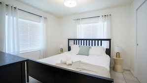 Un dormitorio con cama, mesitas de noche, cortinas y una lámpara de techo.