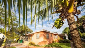 Una casa con fachada de ladrillo, rodeada de abundante vegetación y una palmera con plátanos verdes.