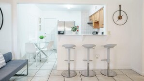 Una cocina moderna con una isla central, taburetes de bar y un comedor con mesa y sillas de vidrio.