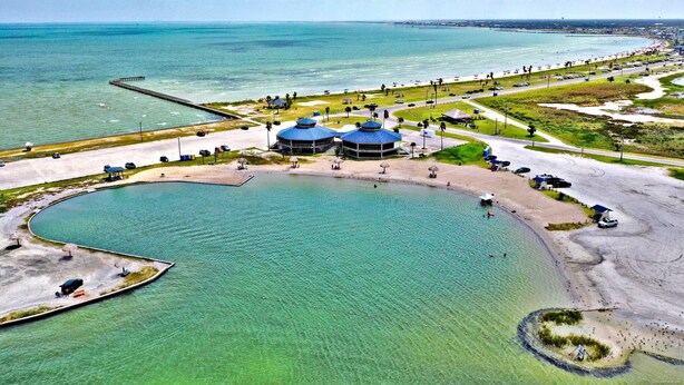 Una zona costera con una extensa masa de agua, un muelle y una playa con sombrillas y algunas personas.