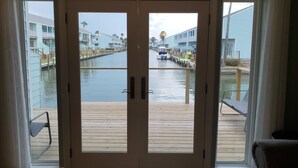 Vista a través de puertas de vidrio que dan a una terraza de madera con un puerto deportivo al fondo.