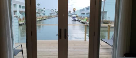 Blick durch Glastüren auf ein Holzdeck mit einer Marina im Hintergrund.