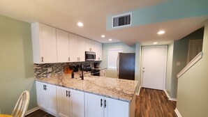 Una cocina moderna con gabinetes blancos, encimeras de granito, un refrigerador negro y un microondas.
