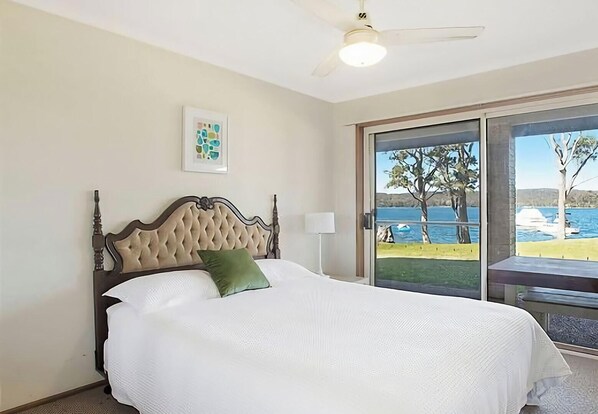 A bedroom with a bed, a ceiling fan, a window with a view of the sea, and a framed picture on the wall. - The Waterfront - Close to shops, club, boat ramp! (Gwandalan)