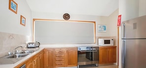 A kitchen with wooden cabinets, a stainless steel sink, a microwave, a stove, and a refrigerator. - The Waterfront - Close to shops, club, boat ramp! (Gwandalan)