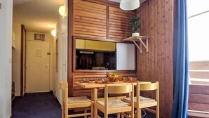 A compact kitchen with wooden cabinets, a built-in oven, and a dining area with a table and chairs. - Le Borsat (Val Claret) by Interhome (Tignes)