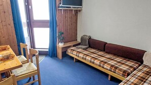 A room with a wooden table, two chairs, a sofa, a small desk, and a television mounted on the wall. - Le Borsat (Val Claret) by Interhome (Tignes)