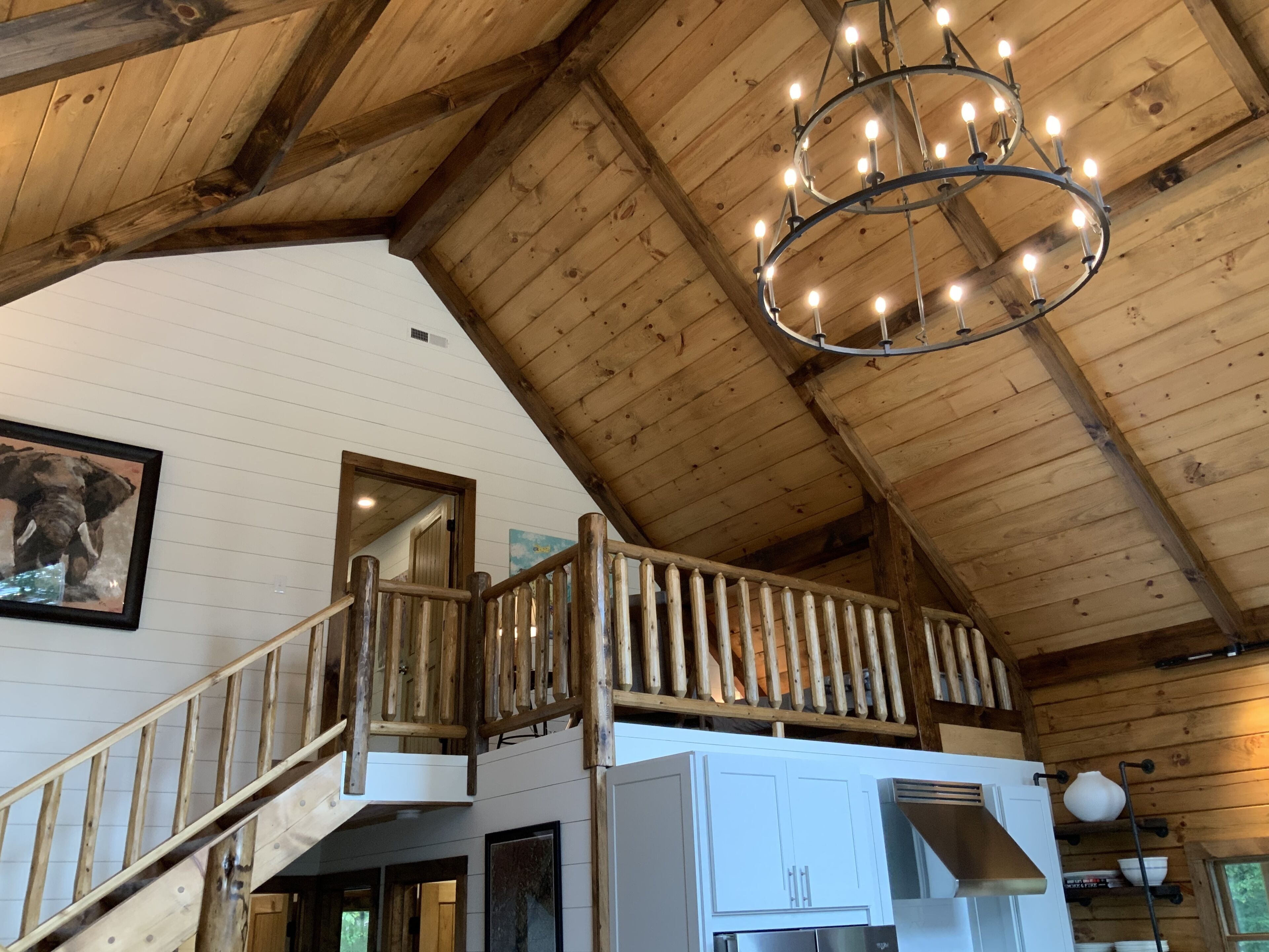 A wooden interior with a staircase leading to a balcony, a chandelier, and a kitchen area.