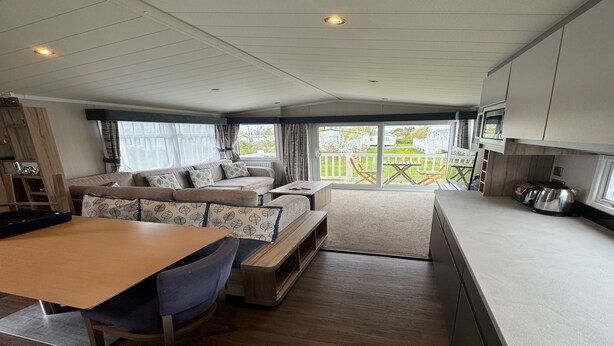 A spacious living area with a sofa set, a dining table, and a kitchen area.