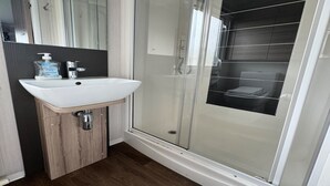 A modern bathroom with a glass-enclosed shower, a white sink, and a wooden cabinet.
