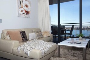 A living room with a sofa, a coffee table, and a view of a body of water through large windows.