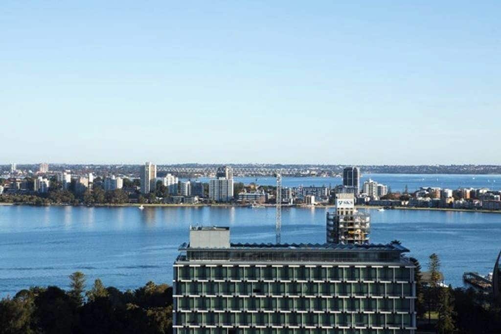 A high-rise building with a grid-like facade, situated near a body of water with a cityscape in the background.