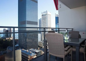 A balcony with a table and chairs, overlooking a cityscape with tall buildings.