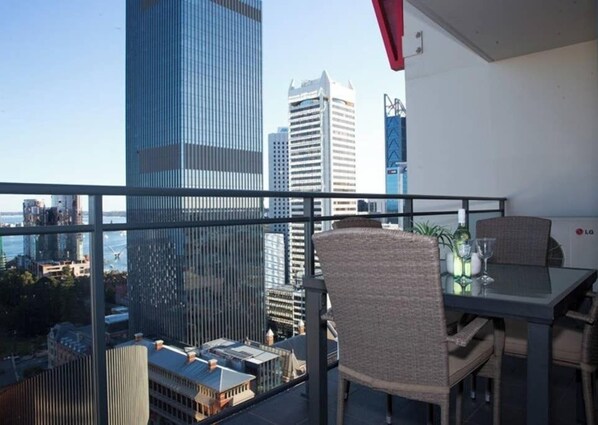 A balcony with a table and chairs, overlooking a cityscape with tall buildings.