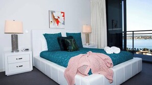 A modern bedroom with a large bed, two bedside tables, a view of the sea, and a balcony. - Central CBD EXEC Stunning View Wifi Netflix Wine (Perth)