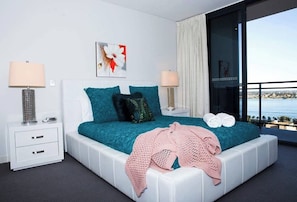 A modern bedroom with a large bed, two bedside tables, a view of the sea, and a balcony.