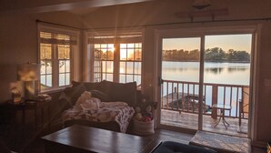 Un salon chaleureux avec une grande fenêtre donnant sur un lac, une table en bois et un canapé confortable.