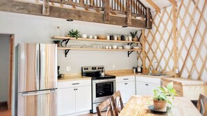 Una cocina con armarios blancos, una mesa de comedor de madera y una escalera con barandilla de madera.