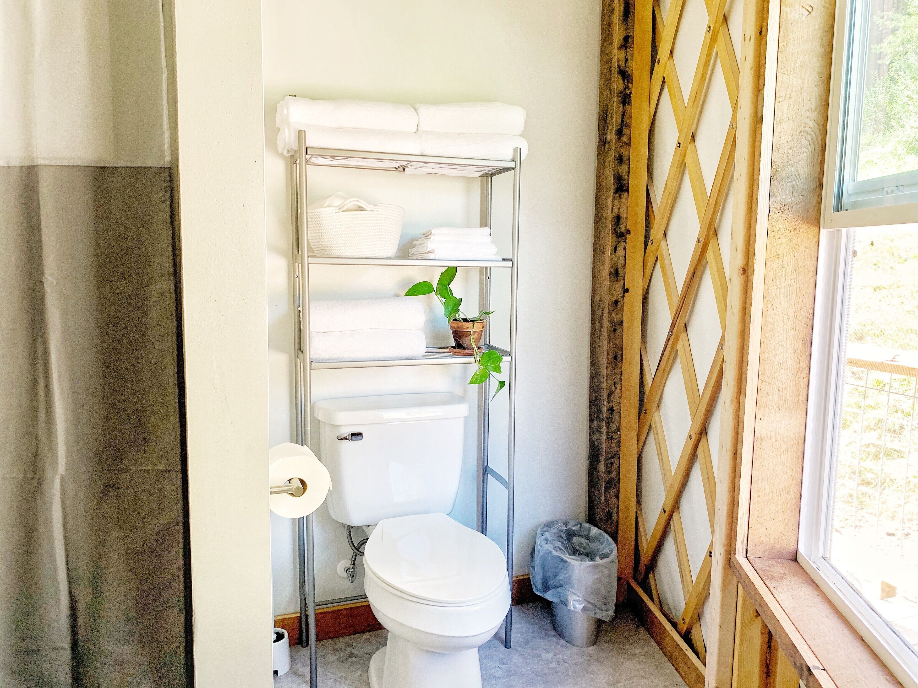 Een badkamer met toilet, een plank met handdoeken, een kamerplant en een raam met houten spijlen.
