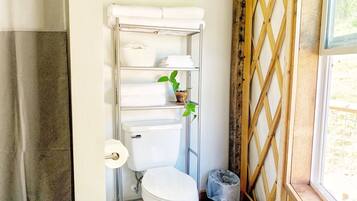 Een badkamer met toilet, een plank met handdoeken, een kamerplant en een raam met houten spijlen.
