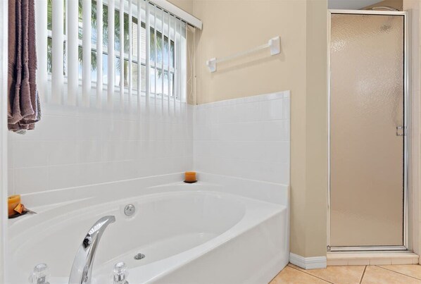 A bathroom with a white bathtub, a glass shower enclosure, and a window with blinds.