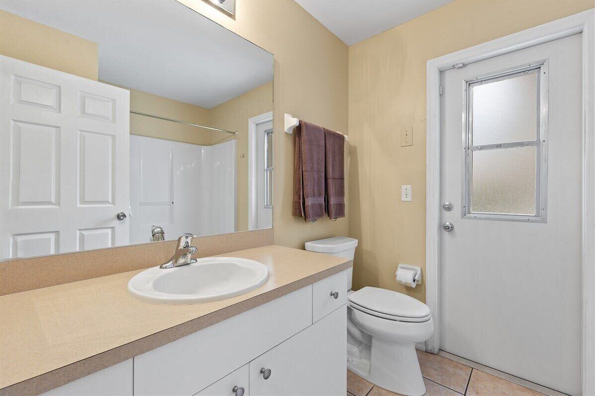 A bathroom with a sink, mirror, toilet, and a door.