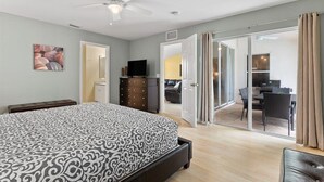 Een slaapkamer met een bed, een dressoir, een televisie en een schuifdeur naar een balkon.