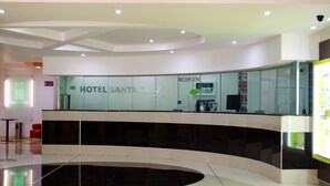 Ein moderner Hotel-Empfangsbereich mit Glasfassade, einer Rezeption und einem digitalen Bildschirm.
