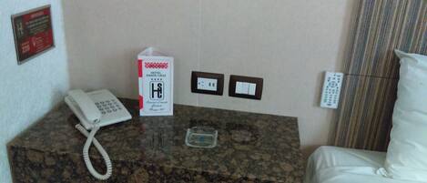 Habitación de hotel con encimera de mármol, teléfono blanco, vaso de agua, control remoto y cama con ropa blanca.