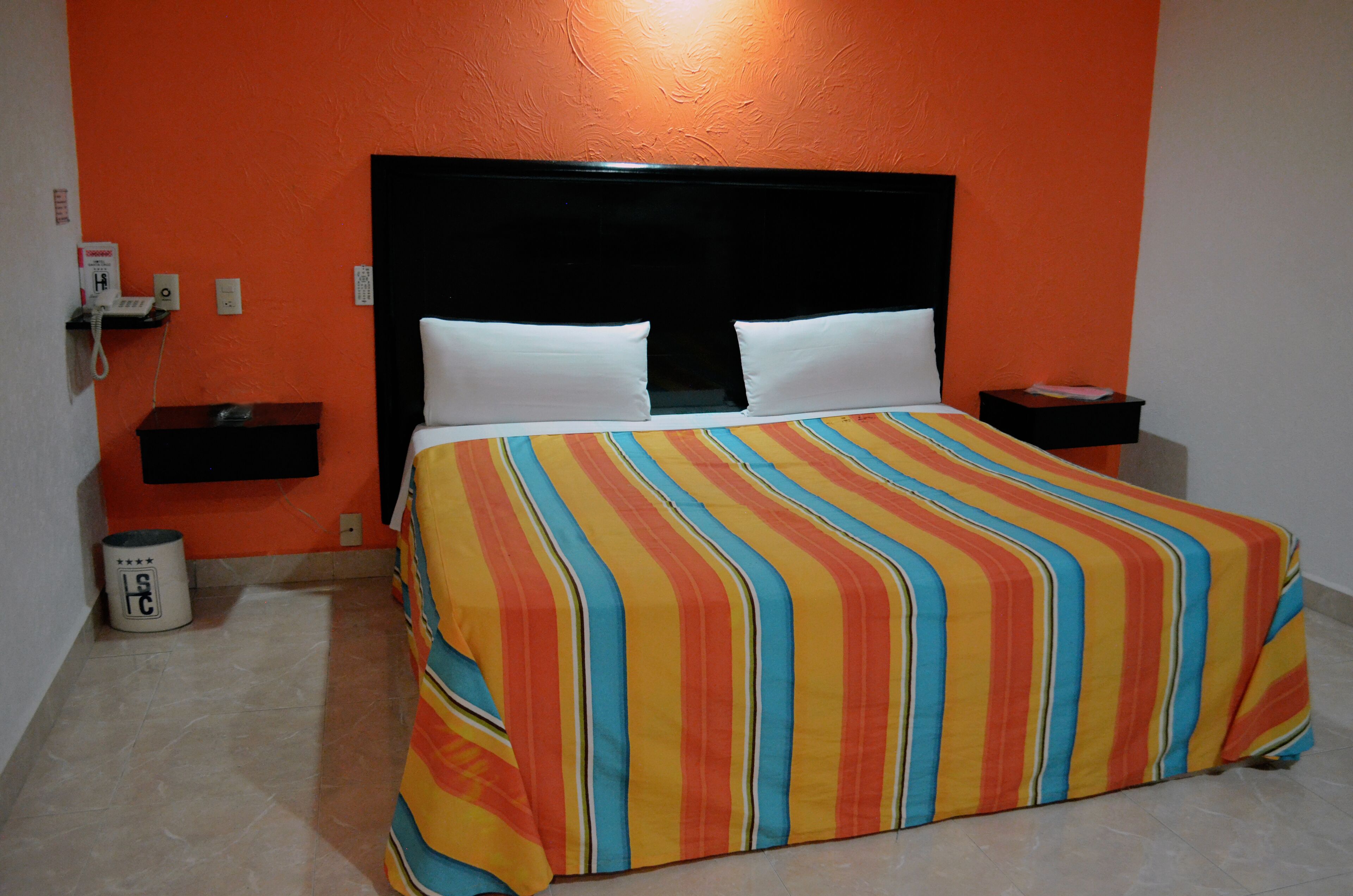 A hotel room with a bed, a nightstand, a trash can, and a wall-mounted phone.