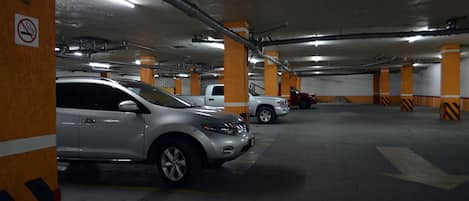 Un estacionamiento de varios niveles con automóviles estacionados en espacios designados, pilares de concreto y flechas direccionales en el suelo.