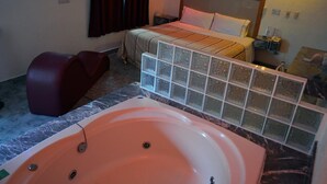 Ein Hotelzimmer mit einer großen Badewanne, einem Bett mit Holz Kopfteil, einem roten Sessel und einem Marmorboden.
