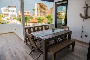 Enjoy the view from this balcony with a table and benches, overlooking the surrounding buildings and palm trees.