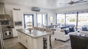 A modern kitchen with white cabinetry, a central island, and a dining area with a white sofa and a black armchair. - Breathtaking Custom Home in Sandy Beach with Great Amenities! (Puerto Penasco)