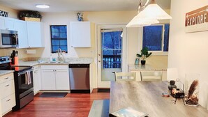A modern kitchen with white cabinets, a wooden dining table, and a view of a snowy deck through a glass door.