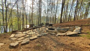A stone fire pit with seating and a table in a forested area.