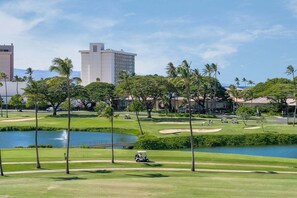 Ein Golfplatz mit einem Wasserhindernis, Palmen und Gebäuden im Hintergrund.