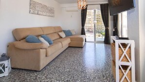 Ein Wohnzimmer mit beiger Couch, Flachbildfernseher, Chandelier und Blick auf Gebäude durch eine Glastür.